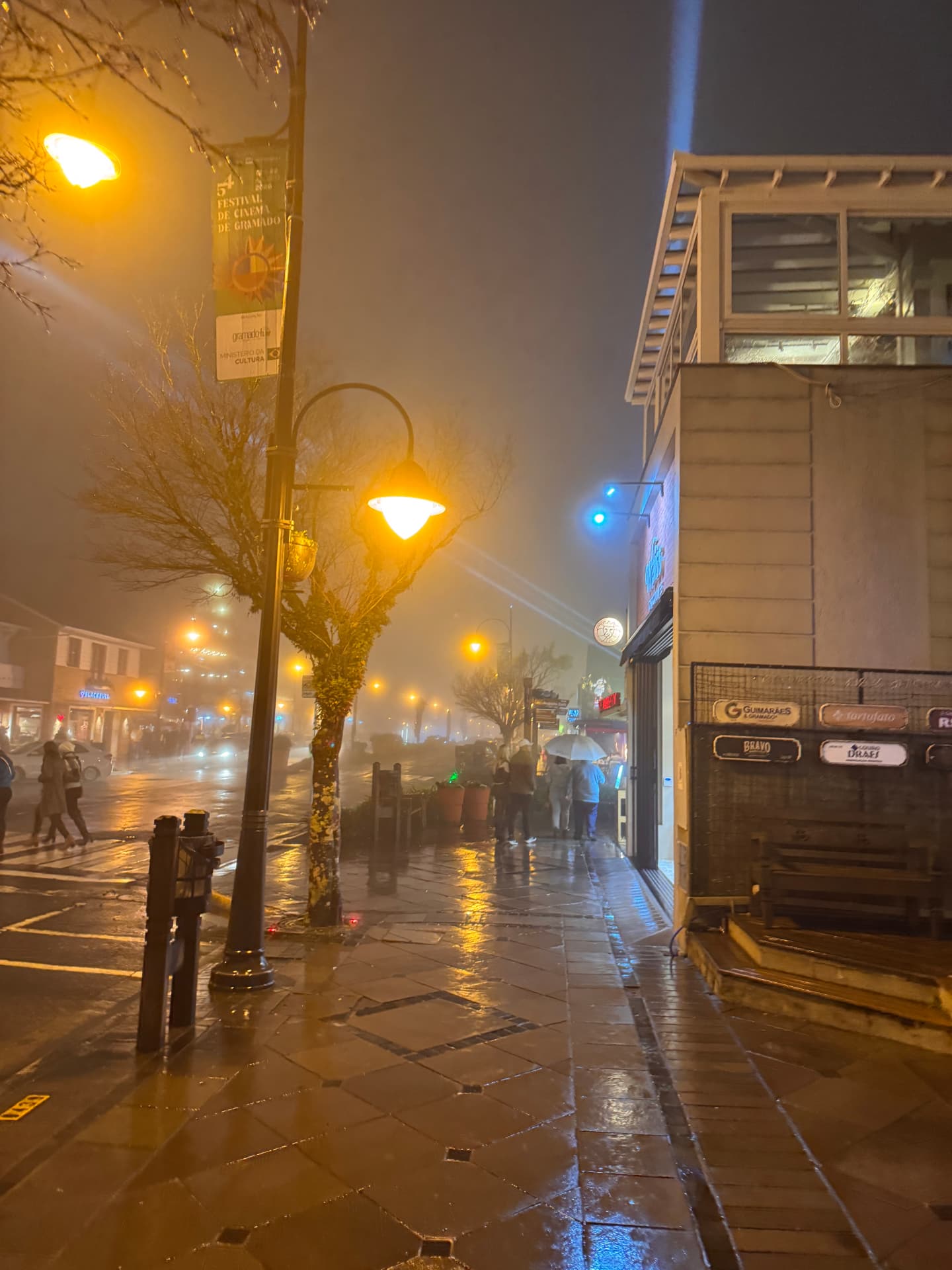 Calçada molhada e luzes do centro de Gramado em noite de neblina